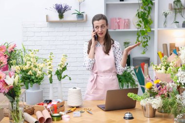 Profesyonel çiçekçi dükkanda çalışırken akıllı telefondan konuşuyor.