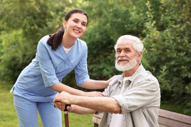 Gülümseyen hemşire ve dışarıda yürüyen bastonlu yaşlı adamın portresi.