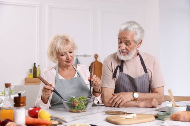 Yaşlı çift mutfaktaki mermer masada birlikte yemek pişiriyor.