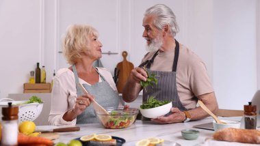 Yaşlı çift mutfaktaki masada birlikte yemek pişiriyor.