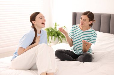 Kadın arkadaşıyla konuşuyor ve evde yatakta gülüyor.