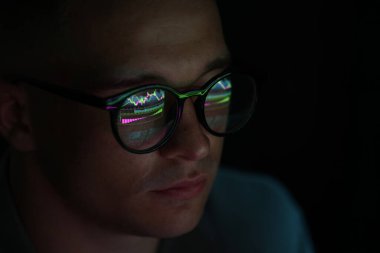 Siyah arka planda yansıması olan gözlüklü genç adam, yakın plan.