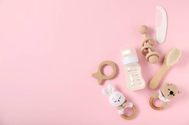 Açık pembe zemin üzerinde süt ve bebek aksesuarları olan bir şişe. Metin için boşluk