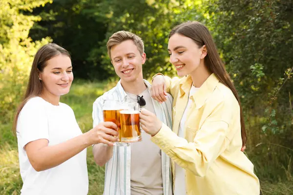 Bir grup mutlu arkadaş dışarıda bira bardaklarını tokuşturuyor.