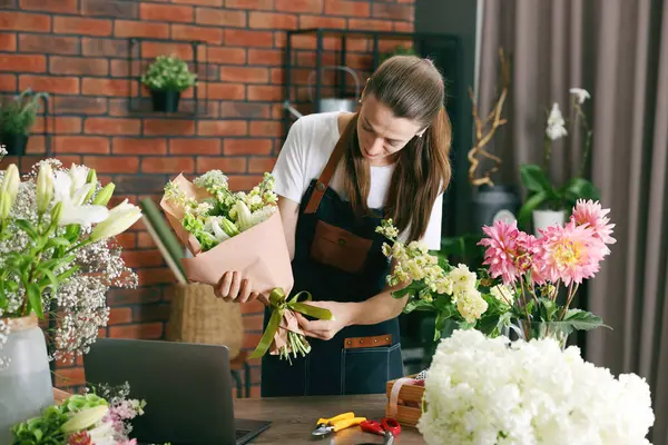 Profesyonel çiçekçi dükkandaki ahşap masada çiçek buketi yapıyor.