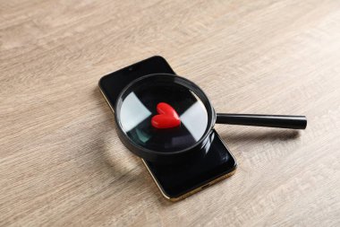 Online flört sitesi. Akıllı telefon, kırmızı kalp ve büyüteç ahşap masanın üstünde.