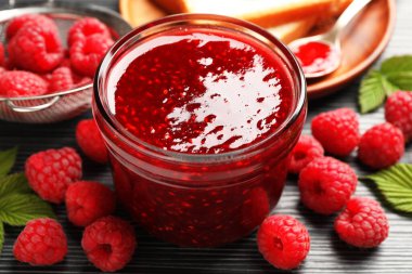 Cam kavanozda tatlı ahududu reçeli ve koyu gri ahşap masada böğürtlen, yakın plan.