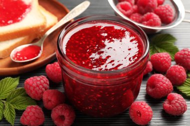 Tatlı ahududu reçeli cam kavanozda, böğürtlen ve ekmek dilimleri koyu gri ahşap masada, yakın plan