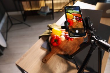 Stüdyoda akıllı telefonla sebze çekmek, ekrana odaklanmak. Profesyonel yemek fotoğrafçılığı.