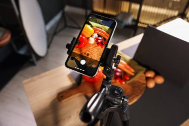 Stüdyoda akıllı telefonla sebze çekmek, ekrana odaklanmak. Profesyonel yemek fotoğrafçılığı.