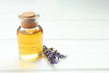 Lavanta yağı ve çiçekler beyaz ahşap masada, yakın plan. Metin için boşluk