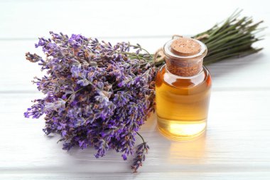 Lavanta yağı ve çiçekler beyaz ahşap masada, yakın plan.