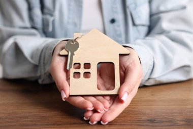 Ev güvenliği. Ev figürlü ve anahtarlı kadın ahşap masada, yakın plan.