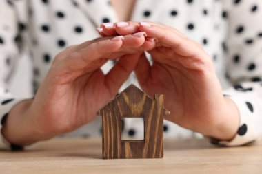 Ev güvenliği. Ahşap masada ev figürlerini koruyan kadın, yakın plan.