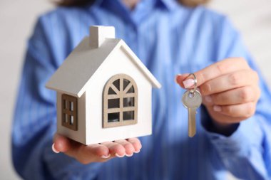 Ev güvenliği. Ev modeli ve anahtarı arka planda olan kadın, yakın plan.