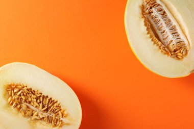 Turuncu arka planda olgun kavun yarımları, düz uzanmış. Metin için boşluk