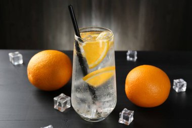 Portakal dilimleri ve siyah ahşap masa üzerindeki buz küpleriyle soda tazeleniyor.