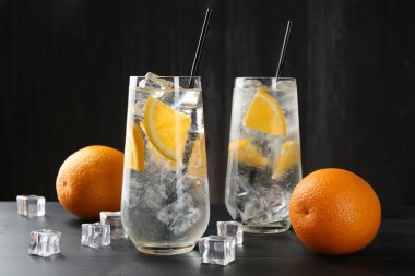 Portakal dilimleri ve siyah ahşap masa üzerindeki buz küpleriyle soda tazeleniyor.