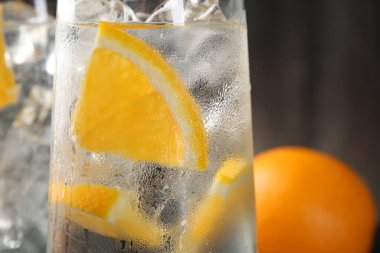 Portakal dilimli soda ve bulanık arkaplanda buz küpleri, yakın plan.