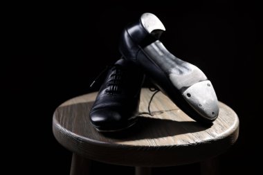 Siyah arka planda tahta taburede step dansı için bir çift ayakkabı, yakın plan.