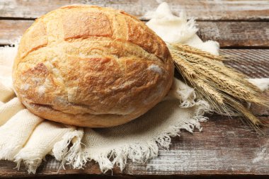 Tahta masada bir somun taze ekmek ve buğday çivisi, yakın plan.