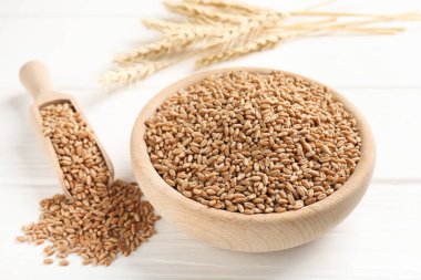 Kasede buğday taneleri, beyaz ahşap masada kepçe ve çiviler, yakın plan.