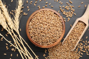 Kâsede buğday taneleri, siyah ahşap masada kepçeler ve çiviler, düz uzanmış.