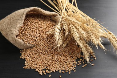 Çuval bezinde buğday taneleri ve siyah ahşap masada çiviler, yakın plan.