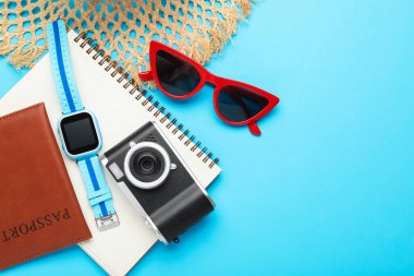 Yaz tatili zamanı. Kamera, akıllı saat, pasaport, defter ve açık mavi arka planda plaj aksesuarları. Metin için boşluk
