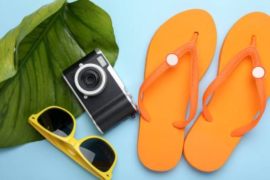 Yaz tatili zamanı. Kamera, yeşil yaprak ve plaj aksesuarları açık mavi arka planda, düz yatar
