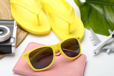 Yaz tatili zamanı. Plaj aksesuarları, pasaport, oyuncak uçak, kamera ve yeşil yaprak beyaz arka planda, yakın plan