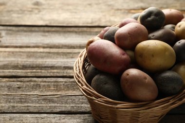 Tahta masadaki hasır sepetin içinde farklı tipte patatesler, yakın plan. Metin için boşluk