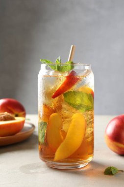 Buzlu şeftali çayı, bardakta nane şekeri ve beyaz masada taze meyveler, yakın plan.