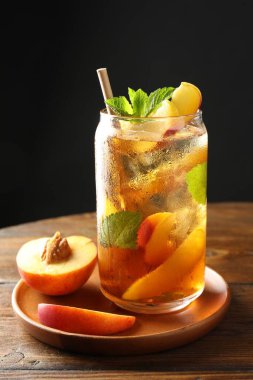 Buzlu şeftali çayını tazeliyorum. Bardakta nane şekeri, ahşap masada siyah arka planda, yakın planda.