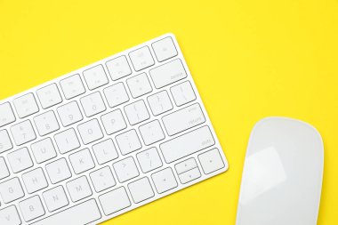 Sarı zemin üzerinde modern beyaz kablosuz klavye ve fare, üst görünüm