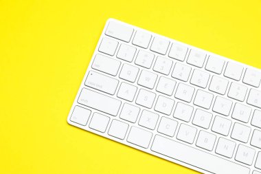 Sarı arka planda modern beyaz kablosuz klavye, üst görünüm. Metin için boşluk