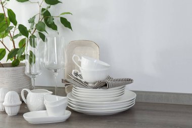 Mutfaktaki tezgahta farklı beyaz bulaşık takımları, bardaklar ve bitkiler var.