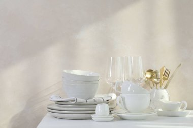 Mutfaktaki tezgahta farklı beyaz bulaşık takımları ve bardaklar var.