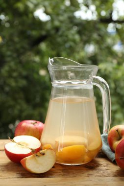 Cam sürahide lezzetli bir karışım ve açık havada tahta masada taze elmalar.