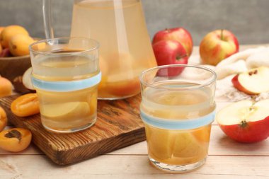 Bardaklar, sürahiler, taze kayısılar ve elmalar ahşap masada, yakın plan.