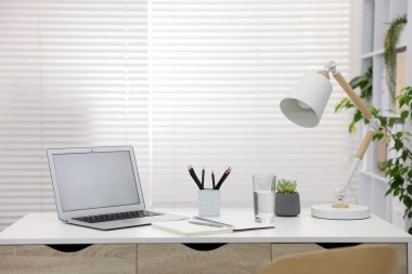 Ofisteki beyaz masada dizüstü bilgisayarı ve kırtasiyesi olan şık bir iş yeri.