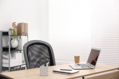 Ofisteki ahşap masada dizüstü bilgisayarı, kahvesi ve kırtasiyesi olan şık bir iş yeri.