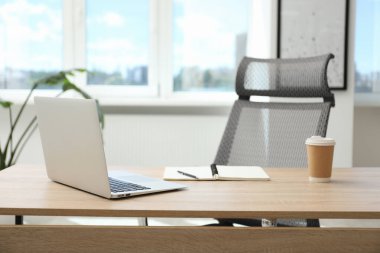 Ofisteki ahşap masada dizüstü bilgisayarı, kırtasiyesi ve kahvesi olan şık bir iş yeri.