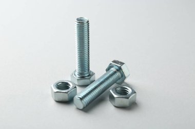 Metal civatalar ve fındıklar beyaz arka planda, yakın plan. Donanım aracı