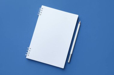 Mavi arka planda beyaz defter ve kalem, üst manzara. Metin için boşluk