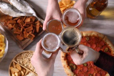 Arkadaşlar beyaz ahşap masada bira bardaklarını tokuşturuyor.