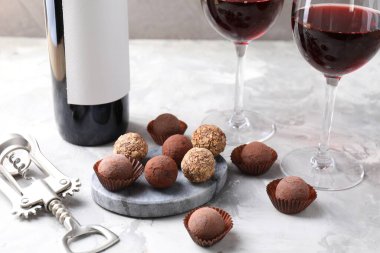 Açık gri arka planda lezzetli trüf şekerleri ve kırmızı şarap, yakın plan.