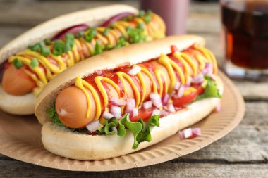 Ahşap masada soslu, marullu ve soğanlı lezzetli sosisliler, yakın plan.