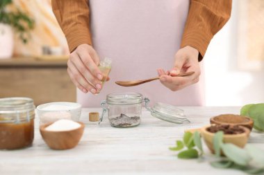 Doğal temizlik yapıyorum. Beyaz ahşap masada kavanoza gerekli yağı koyan kadın, yakın plan.