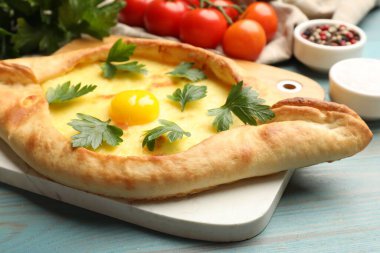 Peynirli, yumurtalı, maydanozlu, domatesli ve baharatlı leziz khachapuri. Açık mavi ahşap masa, yakın plan.